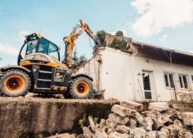 Powerful excavator tearing down an old house during a demolition project outdoors.