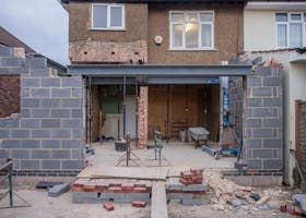 Brick house under renovation with an extension in progress. Visible construction site materials and structure.